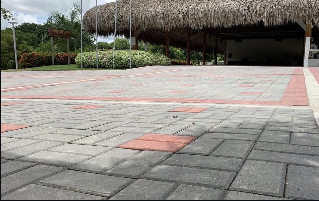 Plaza en adoquines de concreto gris con acentos rojos frente a kiosco de palma